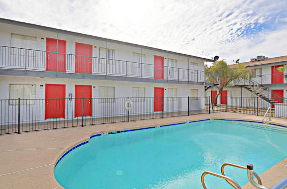 A swimming pool is located in front of a building with red doors.