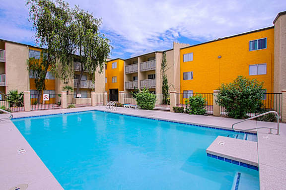 A swimming pool in front of a yellow building.