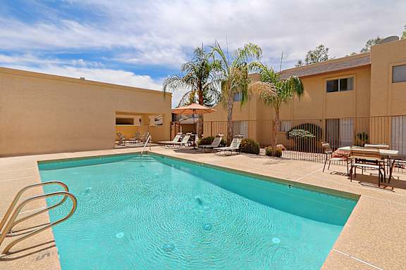 A swimming pool in a backyard with a patio and chairs.
