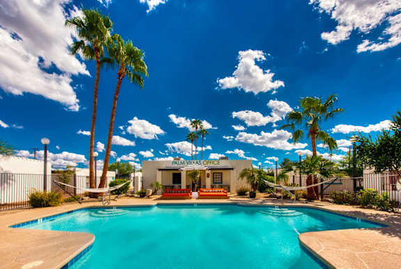 A pool surrounded by palm trees and a white building with the words "Palm VIII Office" on it.