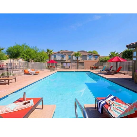 A swimming pool with a red umbrella and a striped towel.