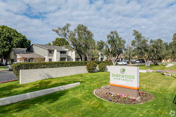 A sign for Sagewood Apartments is in the foreground of a well-kept lawn.
