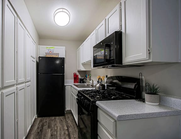 A black refrigerator and microwave in a kitchen with white cabinets.