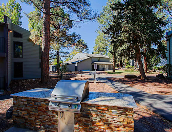 A brick barbecue grill is in the foreground of a residential area with houses and trees in the background.