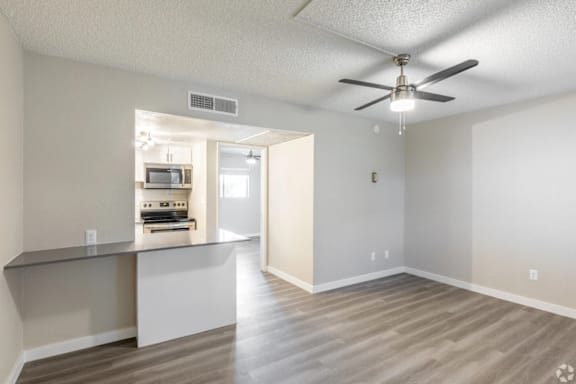 A spacious room with a ceiling fan and a kitchenette in the background.