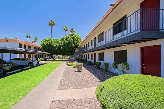 A row of apartments with red doors on the right and covered parking spots on the left at Aspire Mesa in Mesa, AZ 85210