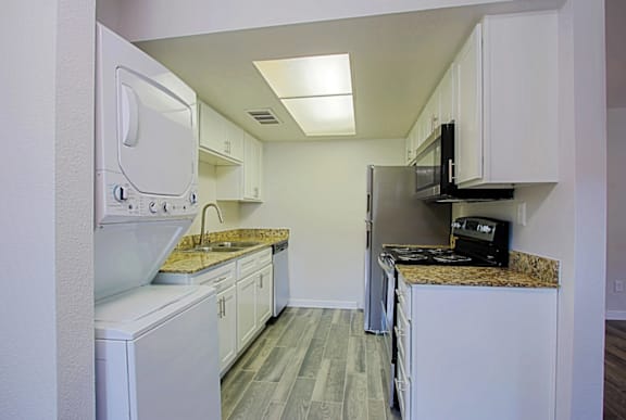 A kitchen with an in-unit washer and dryer,  white cabinets, and granite countertops at Aspire Mesa in Mesa, Arizona