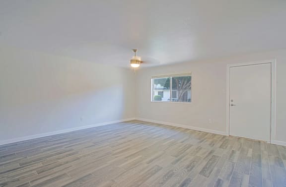 A large room with a window, overhead light with ceiling fan, and plank flooring at Aspire Mesa, Mesa, Arizona 85210