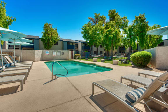 a swimming pool with lounge chairs and umbrellas at Connect on Northern in Glendale, AZ