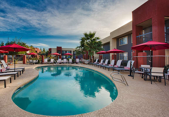 A large outdoor swimming pool surrounded by red umbrellas and lounge chairs.