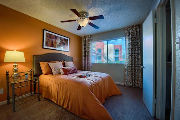 A bedroom with a bed, a fan, and a window with curtains.