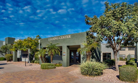 The leasing center is surrounded by greenery and has a clear blue sky above.