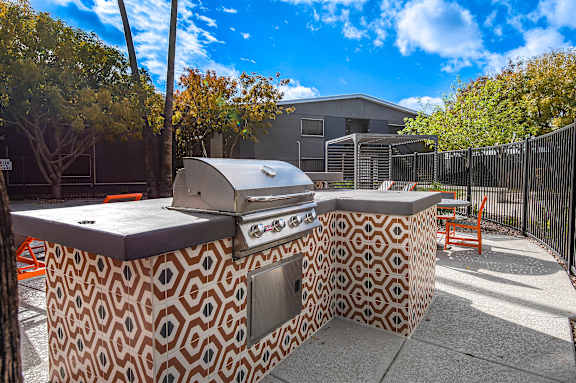 A barbecue grill is on a patterned table in front of a fence.
