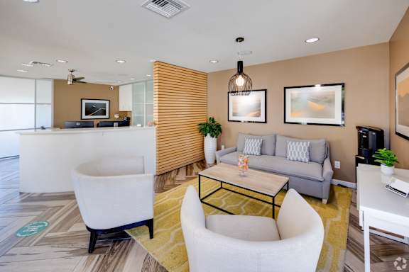 A modern living room with a white chair, a grey couch, and a yellow rug.