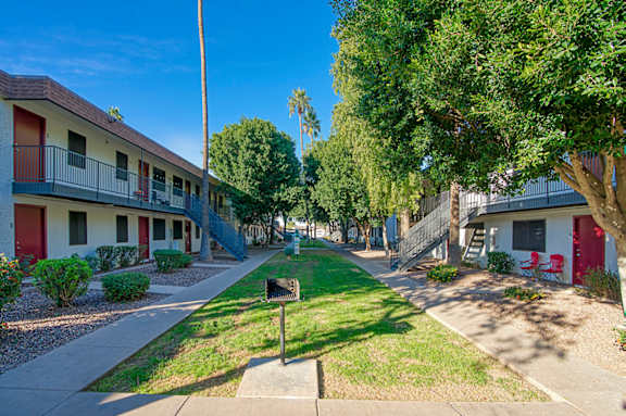 A row of apartment buildings with green trees and bushes in front.