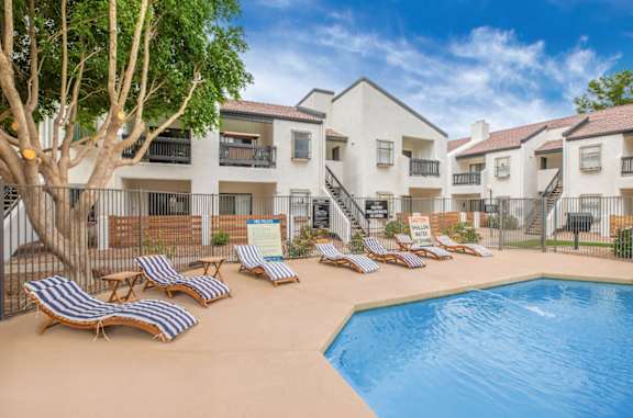 A pool surrounded by lounge chairs and apartment buildings.