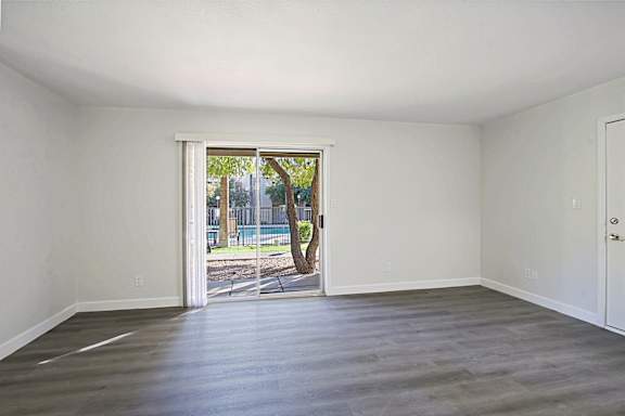 A room with a wooden floor and white walls, with a doorway leading to a backyard.