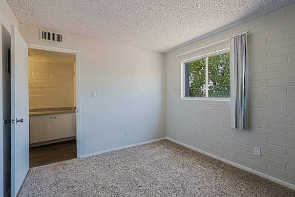 A room with a window and a door leading to a kitchen.