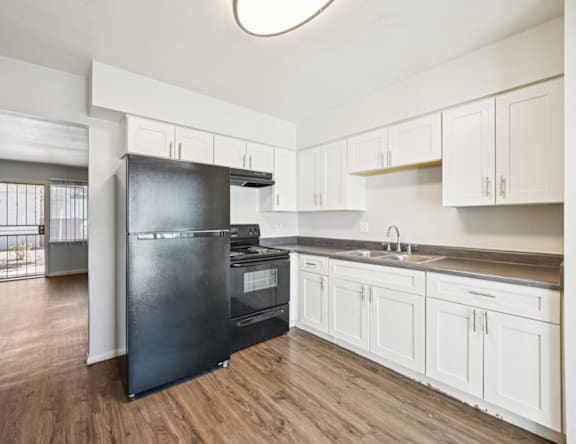 A black refrigerator in a kitchen with white cabinets.