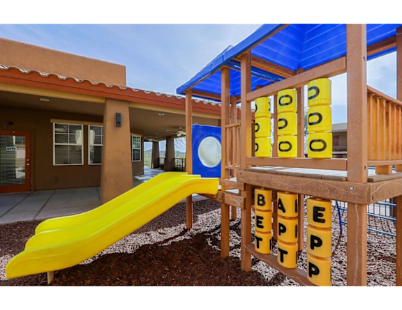 A playground with a yellow slide and a wooden structure with the word "BEEP" spelled out on it.