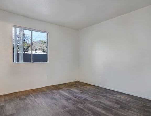 Empty room with a window and wooden flooring.