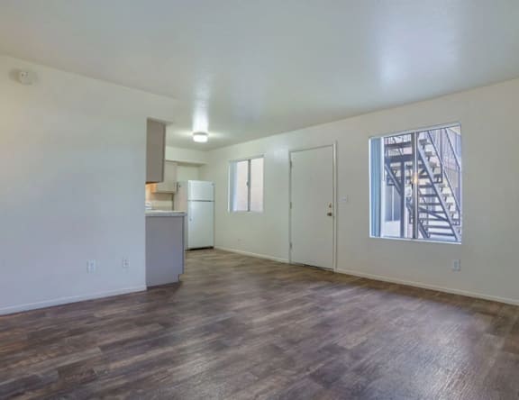 A spacious room with wooden flooring and a staircase visible through the window.
