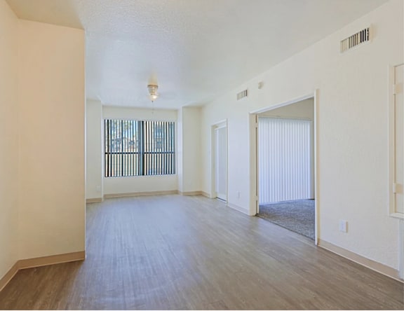 A spacious room with wooden flooring and a large window with blinds.