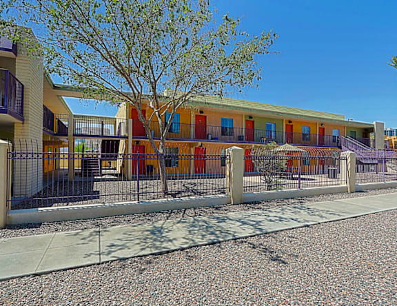 A building with orange doors and windows is surrounded by a metal fence.