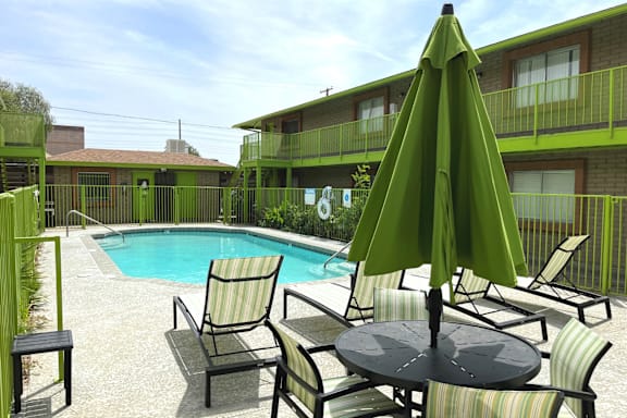 A green umbrella is on a table in the middle of a pool area.