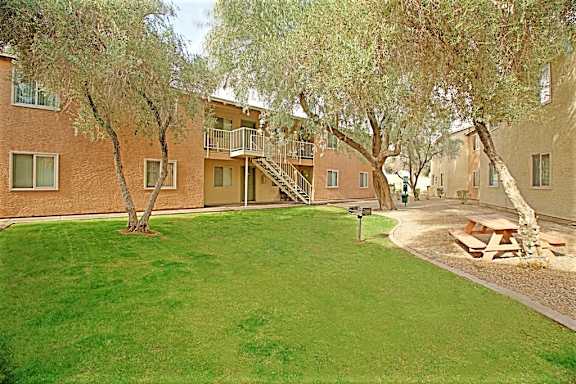 A grassy area in front of apartment buildings with trees.