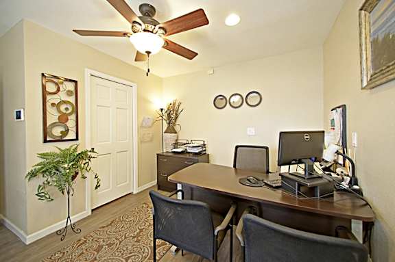 A room with a desk and chairs and a ceiling fan.