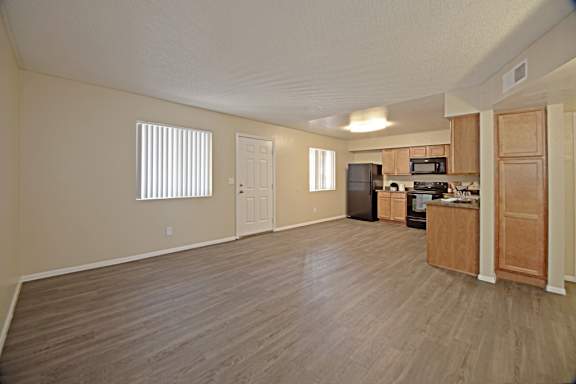 A spacious living room with wood flooring and a kitchen area in the background.