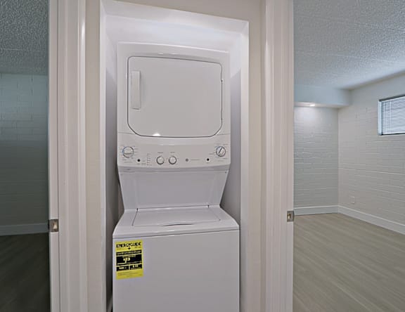 A white dryer is in a small room with a tiled wall.