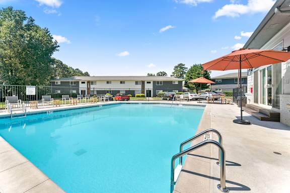 A swimming pool with a red umbrella and a building in the background.