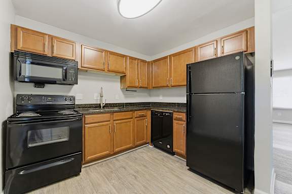 A black refrigerator is in a kitchen with wooden cabinets.