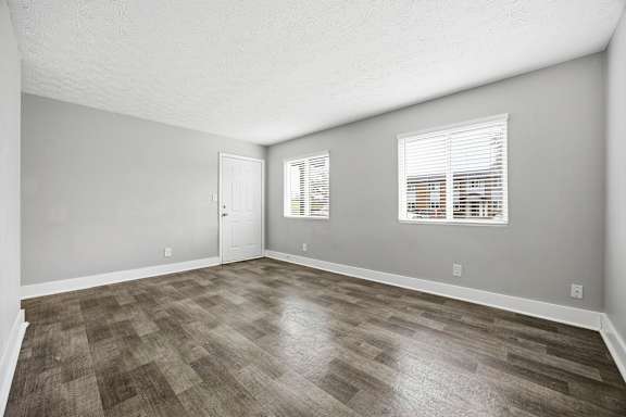 A room with a wooden floor and a window with blinds.