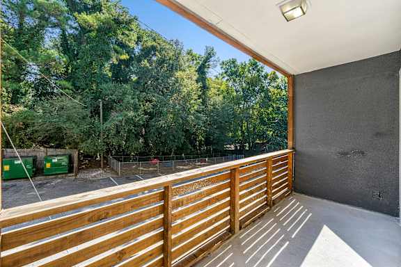 A balcony with wooden slats overlooks a parking lot and trees.