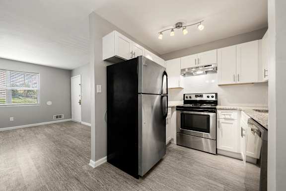 A black refrigerator stands in a kitchen with white cabinets and stainless steel appliances.