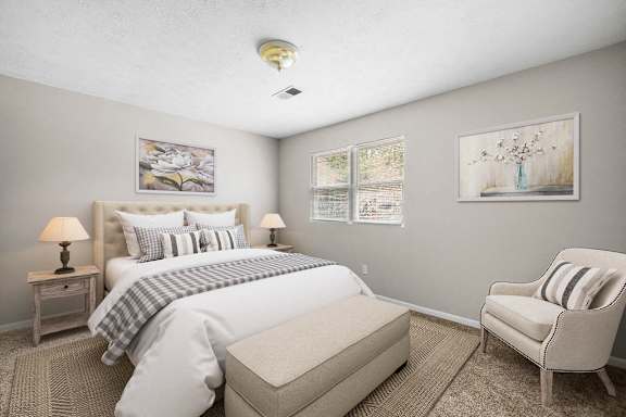 A well-lit bedroom with a large bed, a chair, and a nightstand with a lamp.