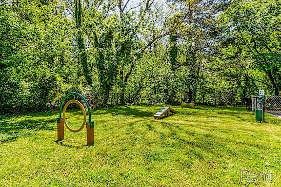 A playground with a green swing set in a grassy area surrounded by trees.