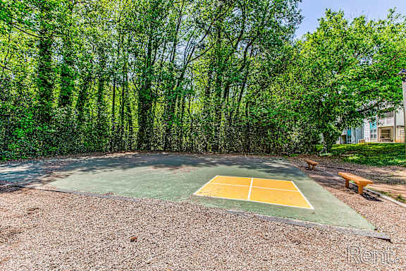 A tennis court surrounded by trees and a bench is visible.