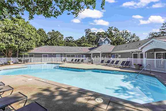 A large outdoor swimming pool surrounded by lounge chairs and trees.
