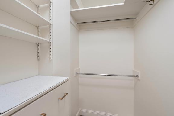 a white walk in closet with shelves and a counter