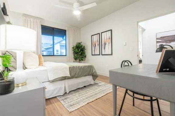 A well-lit room with a bed, desk, and a ceiling fan.