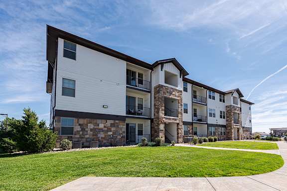 A modern apartment building with a stone facade and a well-maintained lawn in front at Vistas at Jackson Creek, Colorado