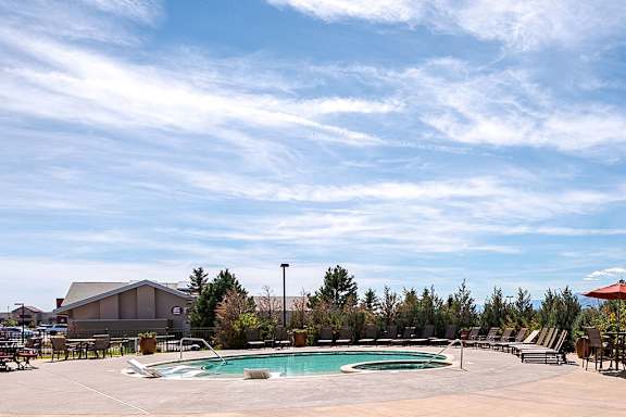 A large outdoor swimming pool surrounded by lounge chairs and umbrellas at Jackson Creek, Monument, Colorado