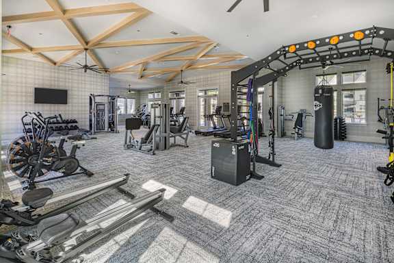 A gym with a variety of equipment including treadmills, weights, and exercise machines at Folksong Apartments, Flowery Branch, Georgia