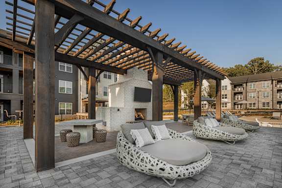 A wooden pergola over a patio with white cushioned seating at Folksong Apartments, Flowery Branch, GA 30542