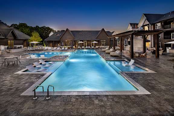 A large swimming pool surrounded by a patio area with chairs and a building in the background at Folksong Apartments, Georgia 30542