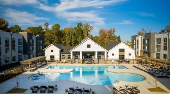 A large swimming pool surrounded by lounge chairs and buildings in the background.